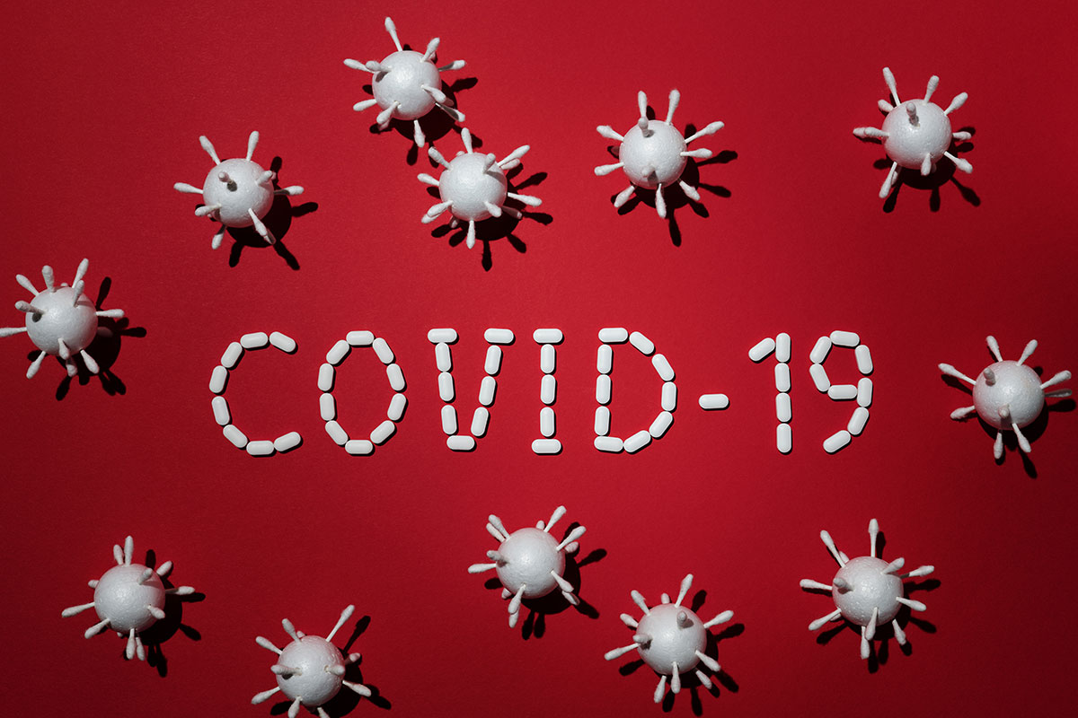 Covid-19 -teksti valkoisista pillereistä punaisella taustalla
